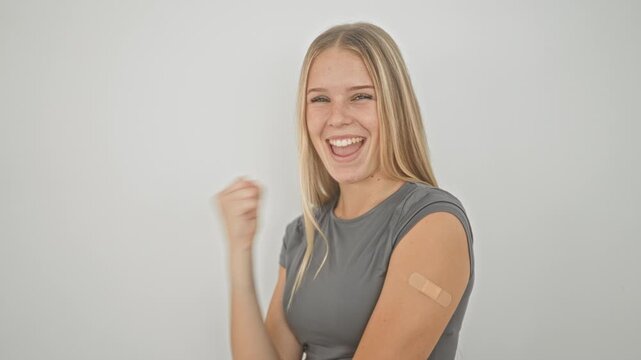 Young woman with bandage on upper arm pumps fist and smiles in studio; vaccination celebration joy hope.