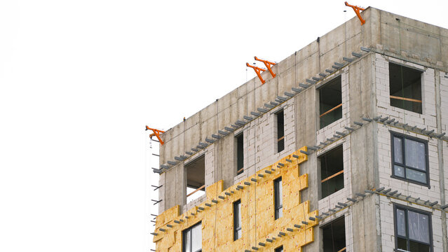Thermal insulation panels being installed on a multistory building facade during construction, showing energy efficient exterior wall finishing and development