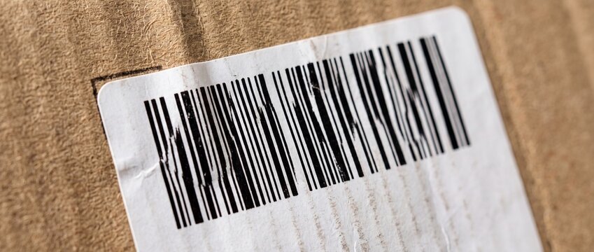 Close up of damaged barcode on white shipping label attached to cardboard package for tracking logistics and delivery services purpose.