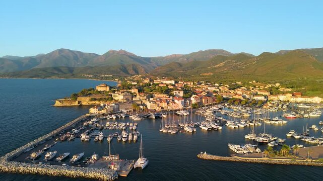 Saint-Florent Corsica drone wide panoramic pull back orbit over marina harbor town, golden hour sunset light, sailboats and coastal mountains bay reveal Cinematic 4K wide panoramic aerial footage