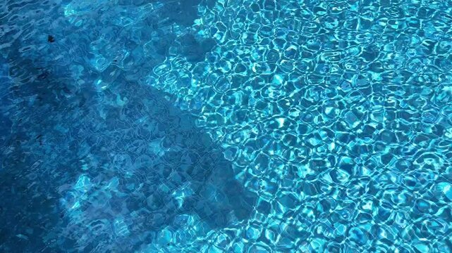 Turquoise pool water with a natural tree shadow drifting across shimmering mosaic tiles, creating organic contrast, ripples and relaxing summer atmosphere. High quality 4k footage