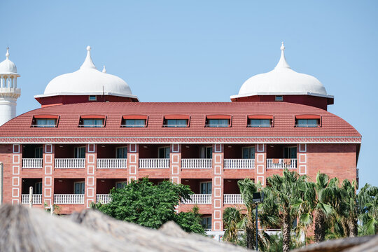 Red resort hotel with domed architecture and palm trees, travel holiday leisure background