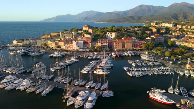 Saint-Florent in Corsica Cinematic 4K drone tracking shot gliding sideways over the marina during warm golden hour. France yachting high end tourism
