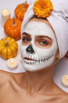 Young woman with Halloween skull mask facial beauty treatment for fall skincare.