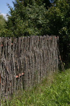 Traditional hand-woven wooden branch fence surrounded by lush green vegetation in a rustic village setting. The natural combination of weathered wood, fresh foliage and rural surroundings conveys an a