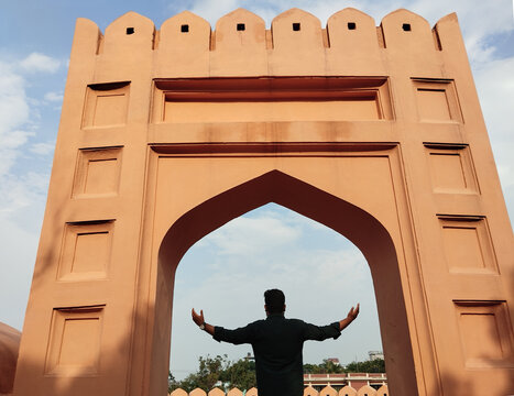 Person standing triumphantly in grand historic archway with open arms under bright sky.