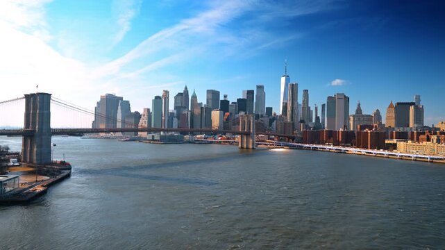 New York, USA, 1 April 2026 : Brooklyn Bridge across the East River and Lower Manhattan. A broad river view places the suspension span below a clear skyline and wispy clouds.