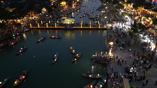 Aerial view of Hoi An Ancient Town at night with illuminated boats on the river and crowds walking along the lantern-lit waterfront in Hoi An, Da Nang, Vietnam.