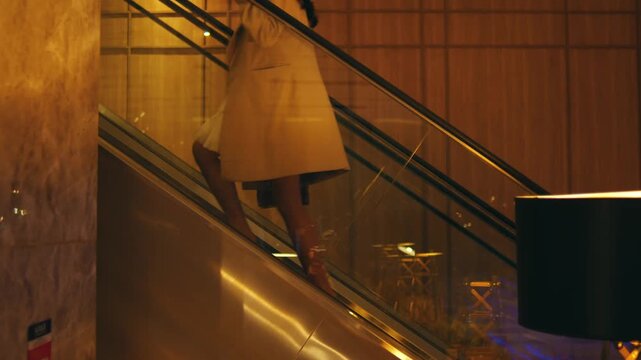 Stylish Woman Riding Up Escalator in Modern Building at Night