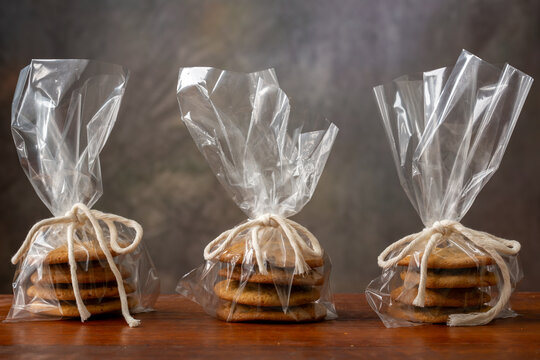 Group of three bags of chocolate chip cookies wrapped in clear plastic with twine tied in a bow displayed on a wooden surface