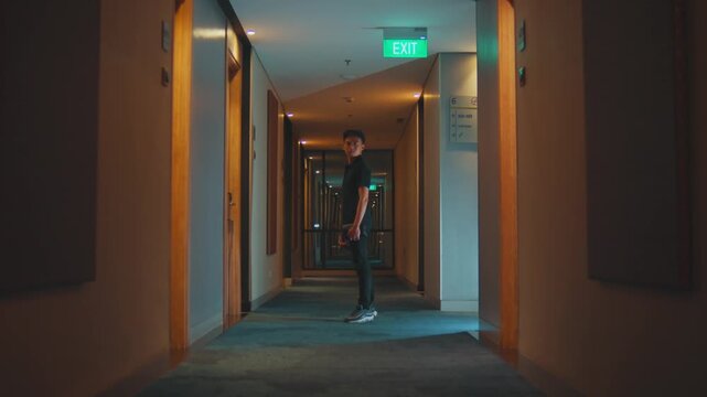Man Stops in Empty Hotel Corridor and Looks Back