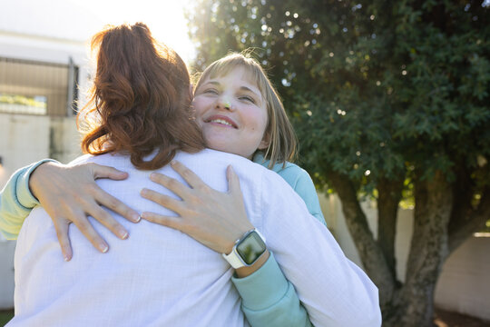 Two women hugging in backyard, wearing light pullover and button-up shirt, showing smartwatch