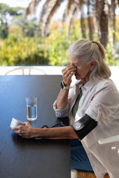 Senior woman sitting on patio at wooden table with blood pressure cuff, holding portable monitor