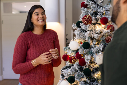 African American couple decorating tree at home, woman in red sweater and gold bracelets