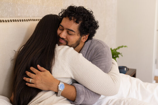 Couple embracing on bed in bedroom, man wearing gray robe showing wristwatch and ring