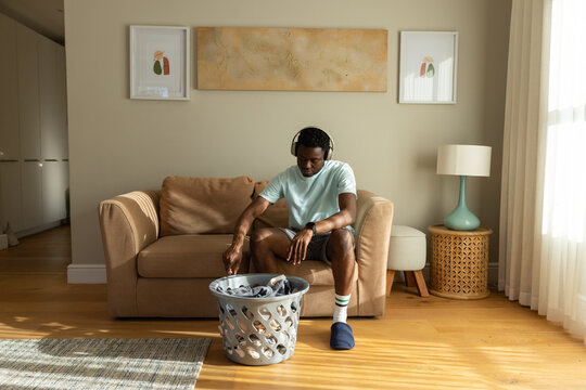 African American man sitting on sofa in sunlit living room reaching toward laundry basket