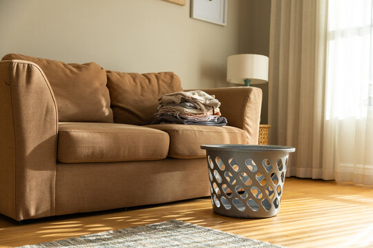 Tan sofa is soaking sunlight in living room corner, folded laundry is resting on right cushion