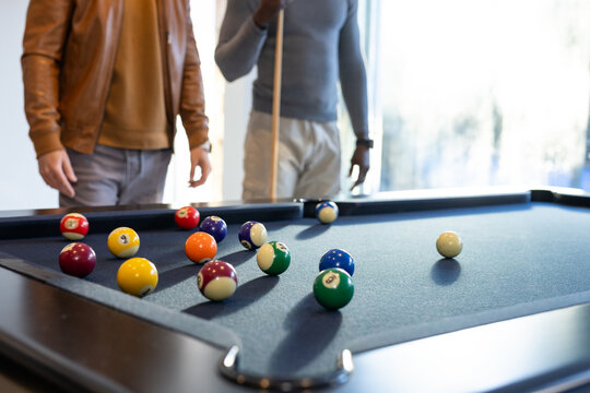Two men holding wooden cue, lining up shot at blue-felt pool table with scattered balls