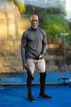 Senior African American man standing on blue court holding paddle and lime ball wearing sportswear