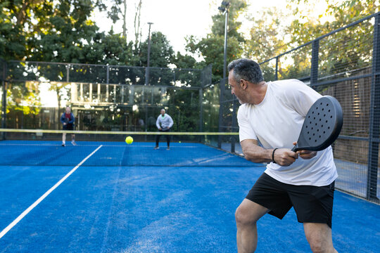 Diverse men playing on court, white-shirted man returning yellow ball with black racket, copy space
