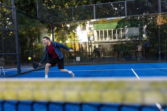 Lunging forward adult male wearing red T-shirt swinging paddle on blue court toward yellow ball