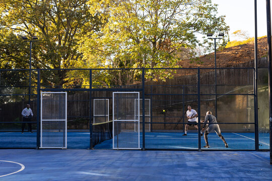 Two males playing on blue padel court in sportswear, holding rackets, yellow ball midair