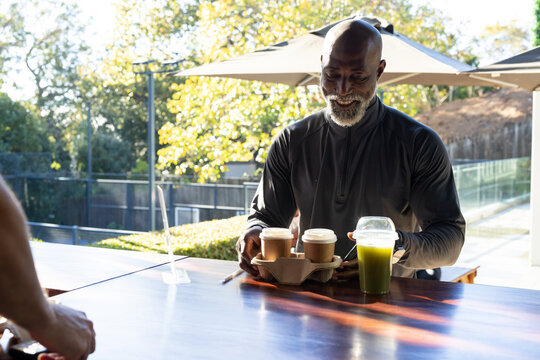 Diverse male friends placing coffee and green juice on patio table with plexi divider