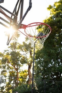 Red basketball rim and white net are glowing with sun flare at outdoor park court