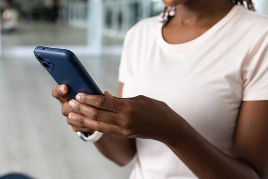 Adult African American woman typing on navy-blue smartphone in lobby, wearing pink tee, band