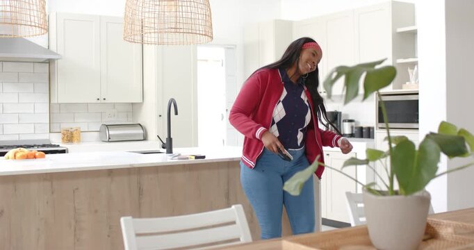 African American woman red headband, jacket entering kitchen adjusting phone cord, dancing to music