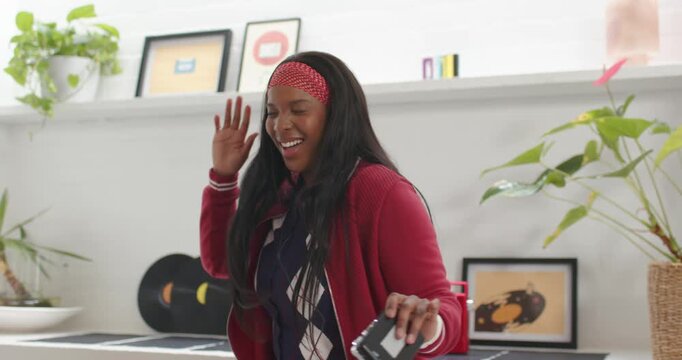 African American woman adjusting red headband grabbing player with wired earbuds grooving at home