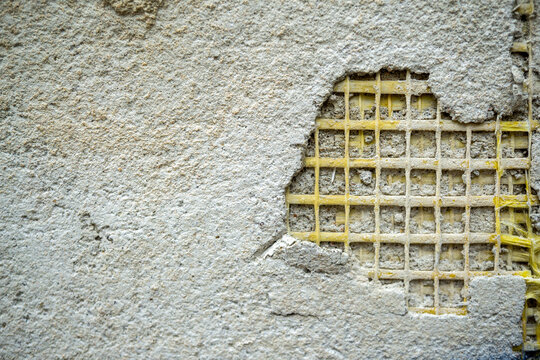 Damaged old stucco wall revealing underlying mesh grid