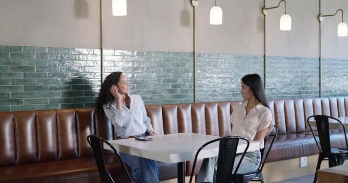 Two women meeting at cafe, sitting at booth, placing purse and phone while server taking notes