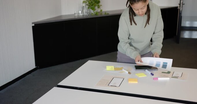 African American nonbinary in green top sorting swatches and sticky notes in meeting room planning