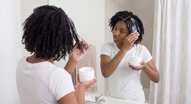 Two women take restorative hair conditioner and cream from a cosmetic jar to apply treatment on curly natural hair