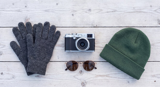 Flat lay of fall travel accessories including retro photo camera knitted grey gloves green beanie hat and sunglasses on white wood boards