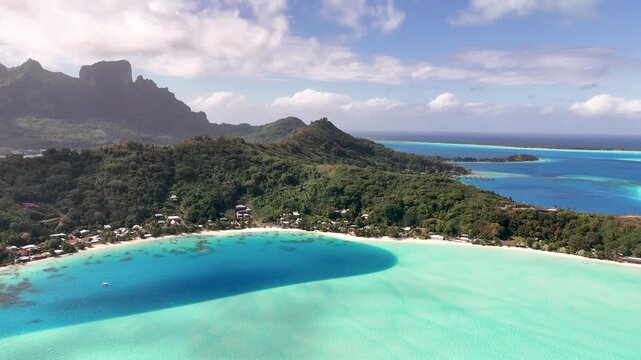 Aerial lateral tracking shot shifting left over the vibrant turquoise lagoon of Matira Beach, revealing the lush tropical coastline and Mount Otemanu in Bora Bora