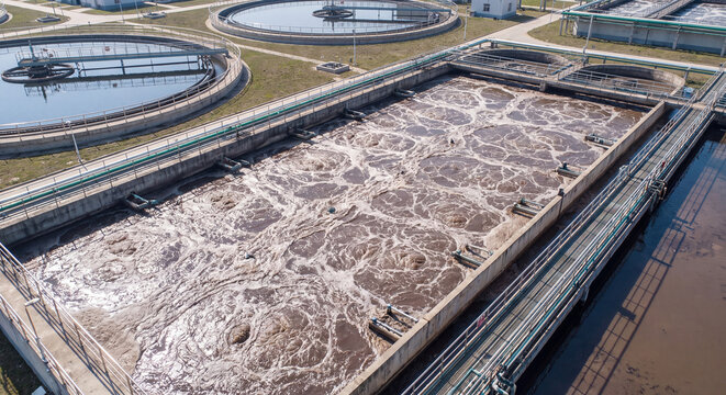 Active aeration basin filled with bubbling foamy water undergoing biological purification stages inside an expansive municipal wastewater treatment plant during daytime