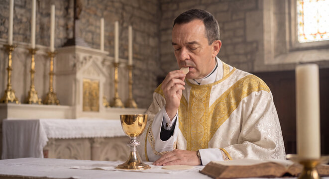 A catholic priest in traditional ceremonial vestments receives the holy sacrament wafer at the altar during a solemn religious liturgy service inside a church
