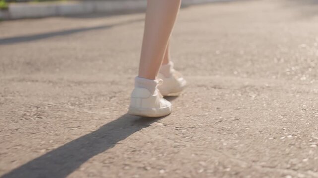 Close up of person legs and feet walking on outdoor path with white sneakers and socks. continuous movement shows rhythmic motion against textured ground capturing natural stride in daylight