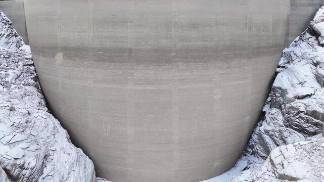 Aerial view of the massive concrete dam structure nestled between steep, snow-covered rocky cliffs in Tafjord, More og Romsdal, Norway.