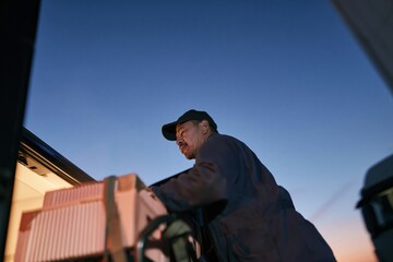 Fototapeta premium Man loading crates into a van at dusk, with visible breath in the cold air, for food bank logistics and winter donation drive campaigns