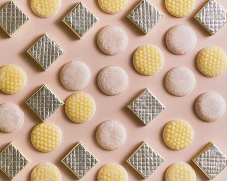 Indian sweets barfi and peda arranged in a repeating grid on a blush pink background, featuring edible silver leaf and powdery textures for packaging design