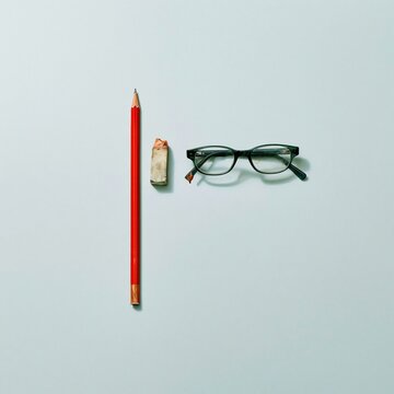 Reading glasses with a red pencil and worn eraser on a cool grey background, featuring smudged lenses and scuffed textures for editing and proofreading services, with copy space