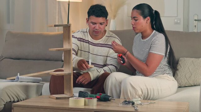 Young woman trying different tools and assembly methods on flat pack furniture until finding the right solution next to her husband in a cozy modern living room home setting