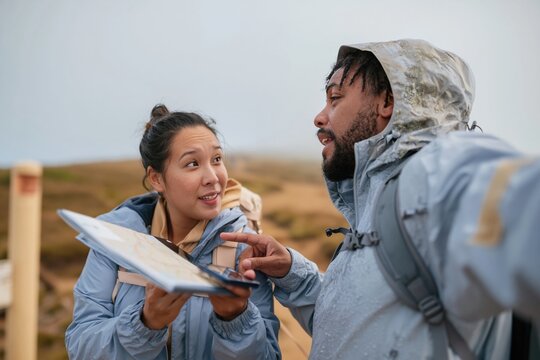 Two hikers discussing a digital map on a phone in a misty field, featuring wet gear and muted tones for navigation and travel apps
