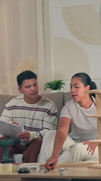 Cheerful young couple sitting on a sofa overcoming a confusing DIY challenge together and actively starting to assemble new flat pack home furniture in a modern living room setting