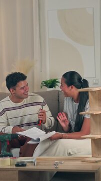 Cheerful young millennial couple sitting together on a sofa and laughing at their mistake while struggling to understand complex flat pack furniture assembly instructions in a cozy modern home