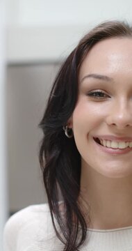 Vertical video: Adult woman blinking, smiling while facing camera at vanity, hoop earring