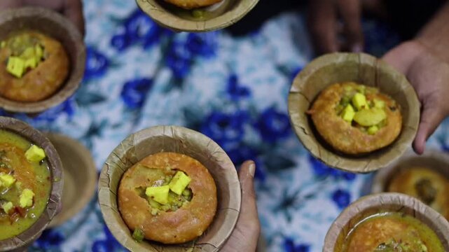 Top-down b-roll footage of multiple hands holding traditional leaf bowls (donas) filled with authentic Indian street food Kachori and Aloo Sabzi, showcasing community eating and festive celebration.
